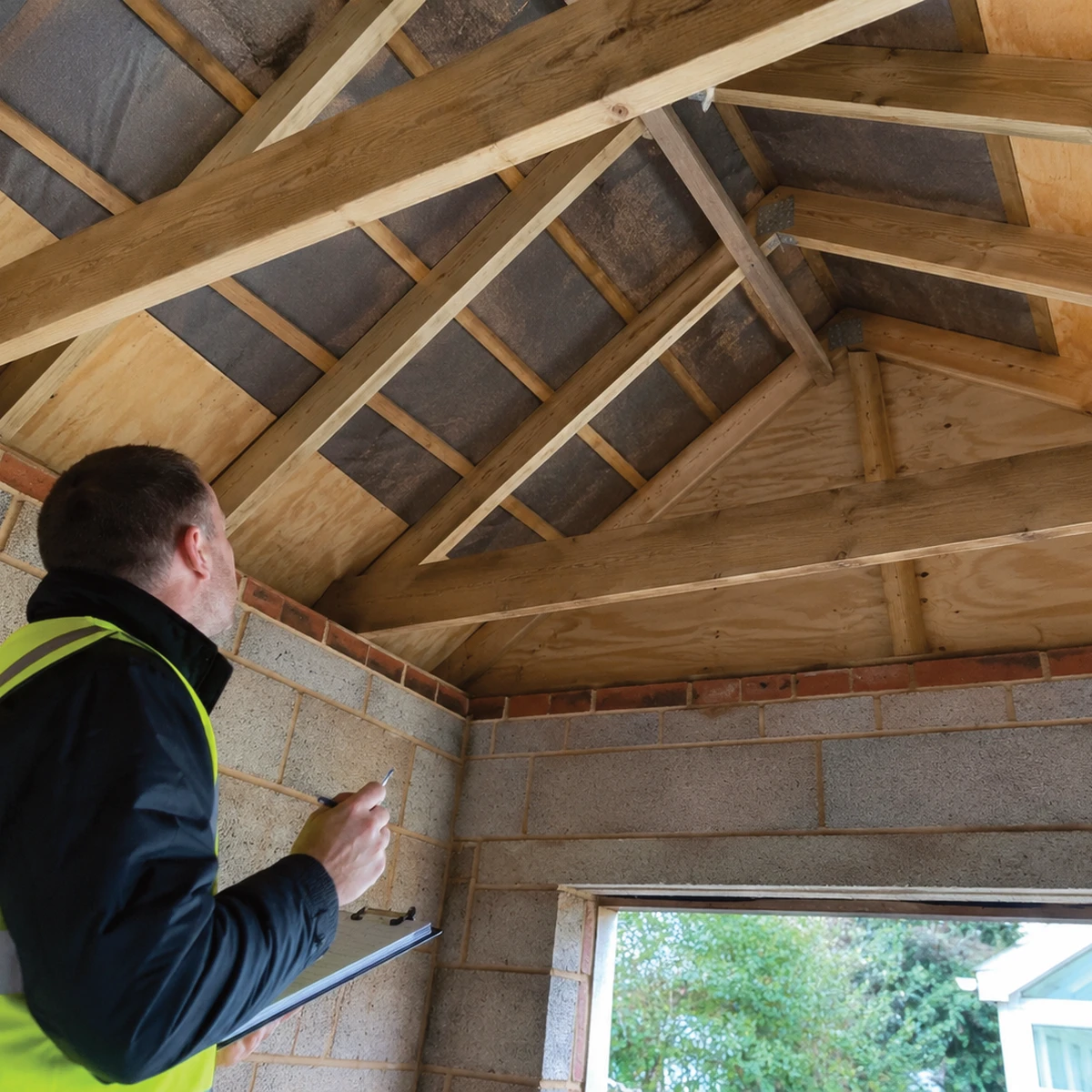 Surveyor inspecting the timber roof structure of a garage or outbuilding before a solar installation.
